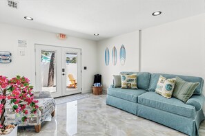 A room with a teal sofa, a door with a glass panel, and a wall with surfboards. - Aqua Tides Cottage #5|1br/1ba steps to beach (Indian Rocks Beach)