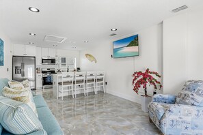 A modern kitchen with white cabinets, a stainless steel refrigerator, and a dining area with white chairs. - Aqua Tides Cottage #5|1br/1ba steps to beach (Indian Rocks Beach)