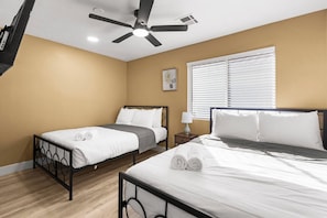 A hotel room with two beds, a ceiling fan, a window with blinds, and a bedside table with a lamp. - Pool & Hot tub • Game Room • King Beds • 22 Guests Max (Las Vegas)