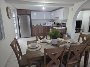 Un comedor con una mesa de madera dispuesta para seis personas, rodeada de sillas. Hay una planta en maceta sobre la mesa.