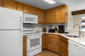 A compact kitchen with wooden cabinets, a white refrigerator, a microwave, a stove, a coffee maker, and a dishwasher. - Spacious 2-bedroom  condo with AC in beautiful Waikiki (Honolulu)