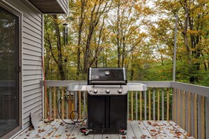 A portable Weber Genesis grill on a wooden deck with a view of autumn trees. - Brown Bear Chalet Game Room Pool Table Fire Pit (Big Bass Lake)