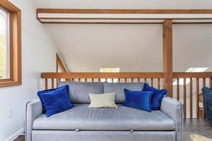 Ein graues Sofa mit blauen und weißen Kissen in einem Raum mit Holzbalken und einer geneigten Decke.