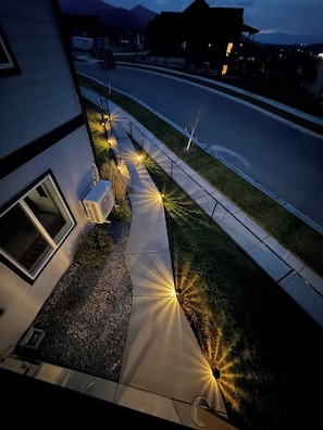 Une rue résidentielle au crépuscule, bordée de maisons des deux côtés, avec un trottoir et un éclairage public.