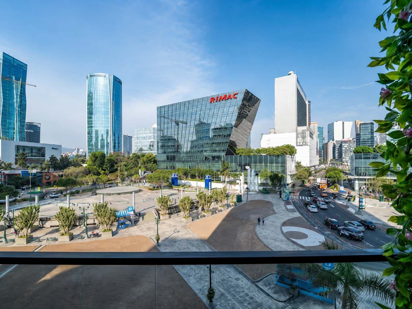 A cityscape with modern buildings, including a prominent RIMAC building, and a busy street with cars and pedestrians.