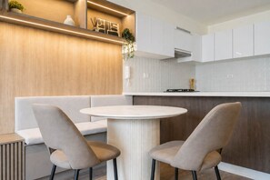 A modern kitchen with a round dining table, two chairs, a built-in bench, and a countertop with a stove. - Executive 2 Escritorios AC Balcón (San Isidro)