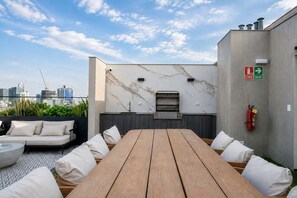 An outdoor seating area with a table and chairs, a built-in grill, and a city skyline view. - Executive 2 Escritorios AC Balcón (San Isidro)