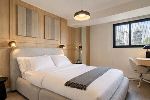 A modern bedroom with a large bed, a desk, and a window with a city view. - Executive 2 Escritorios AC Balcón (San Isidro)