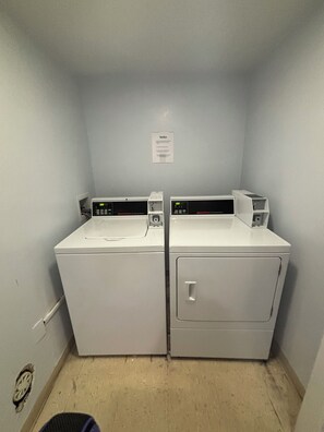 A laundry room with two stacked washers and dryers, a notice on the wall, and a visible drain. - Brand New in October! 2 Bikes to Ride to Beach/Coligny/Pool/Tennis (Hilton Head Island)