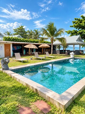 A swimming pool with lounge chairs and umbrellas, surrounded by greenery and a clear sky. - Amana Beach Resort (Bophut)