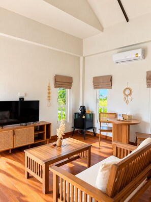 A spacious living area with a flat-screen TV, wooden furniture, a coffee machine, and a wall-mounted air conditioner. - Amana Beach Resort (Bophut)