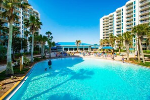 A large swimming pool surrounded by palm trees and hotel buildings. - Pool Views,  2 Bed 2 Bath,Balcony, Lagoon Pool,Shuttle,The Palms of Destin (Destin)