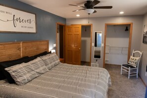 Ein Schlafzimmer mit einem Bett, einem Deckenventilator, einer Tür, einem Sessel und einer Wand mit einem Motivationsspruch.