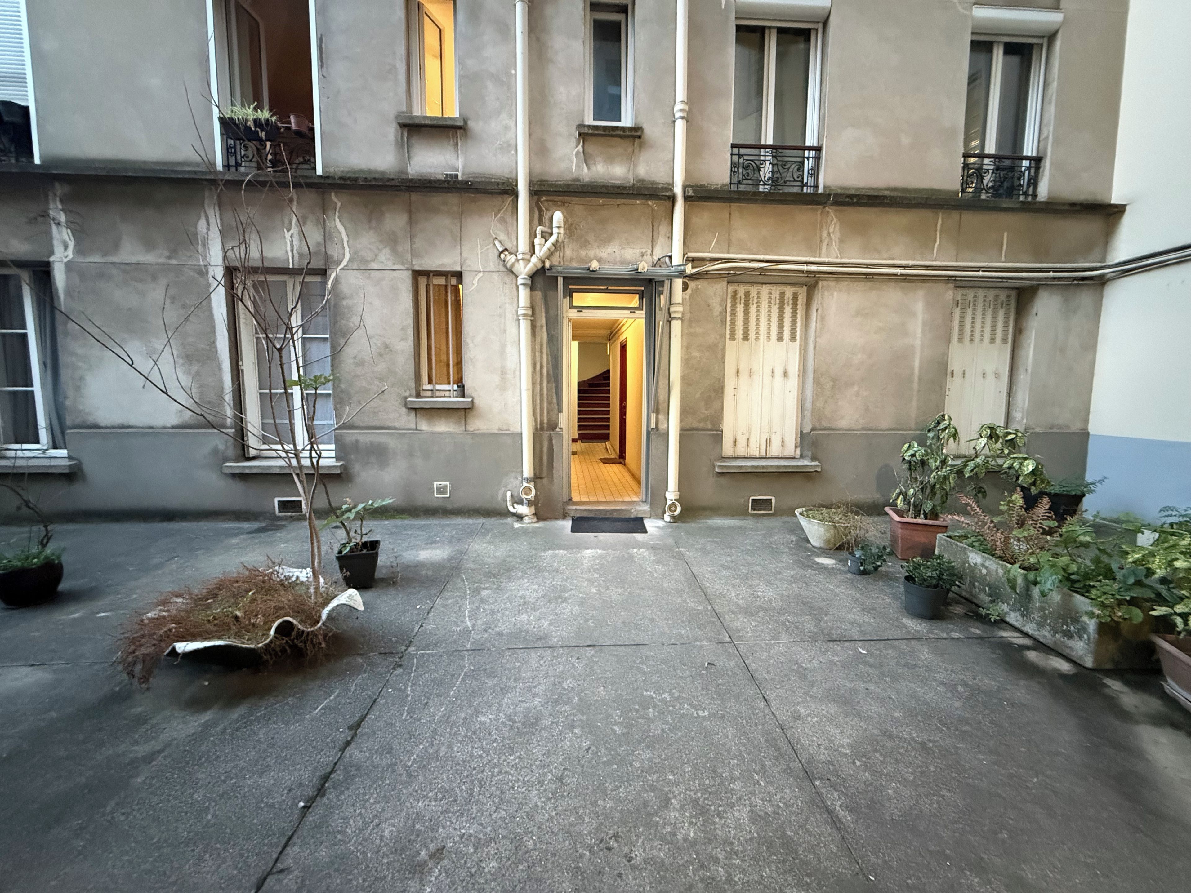 A courtyard with a building entrance, potted plants, and a staircase leading to an upper floor.