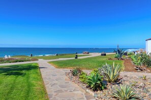 A coastal property with a stone pathway leading to a grassy area with plants and a view of the ocean. - Ocean View Condo -  Pools, Beach Access & More (Playas de Rosarito)
