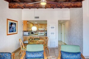 A dining area with wicker chairs and a table, a kitchen with wooden cabinets and a stove, and a hallway leading to another room. - Ocean View Condo -  Pools, Beach Access & More (Playas de Rosarito)
