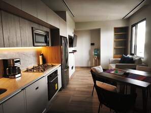 Una cocina moderna con estufa integrada, microondas y refrigerador. Cuenta con una zona de comedor con mesa y sillas, además de un dispensador de agua.