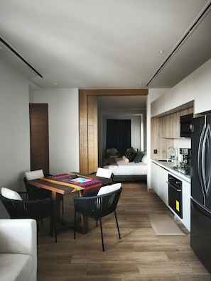 A modern kitchen with a built-in refrigerator, a dining area with a wooden table and chairs, and a bedroom visible through an open door. - NEW BELLA VISTA (Puerto Vallarta)