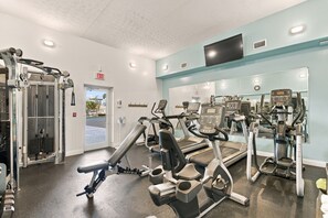 Et fitnesscenter med forskellig træningsudstyr, herunder løbebånd, styrkemaskiner og en spejlvæg.