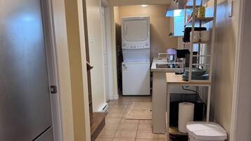 A compact kitchen with a refrigerator, washing machine, and a coffee maker on the counter.