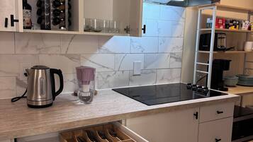 Una cocina moderna con armarios blancos, un hervidor de acero inoxidable, una licuadora y un horno empotrado.