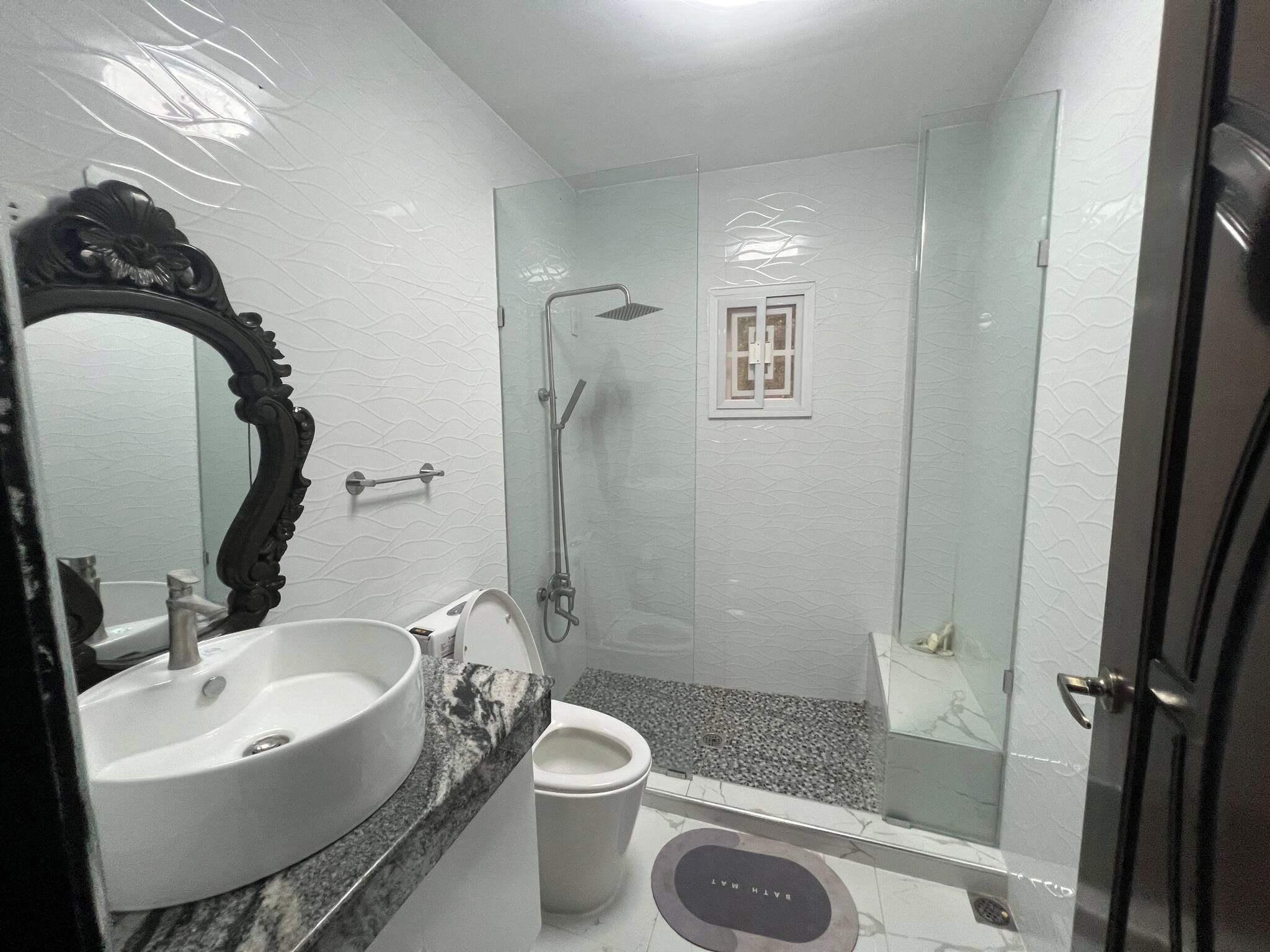 A bathroom with a white sink, a mirror with an ornate frame, a shower with a glass door, and a toilet.