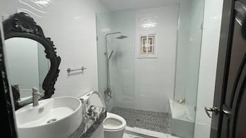 A bathroom with a white sink, a mirror with an ornate frame, a shower with a glass door, and a toilet.