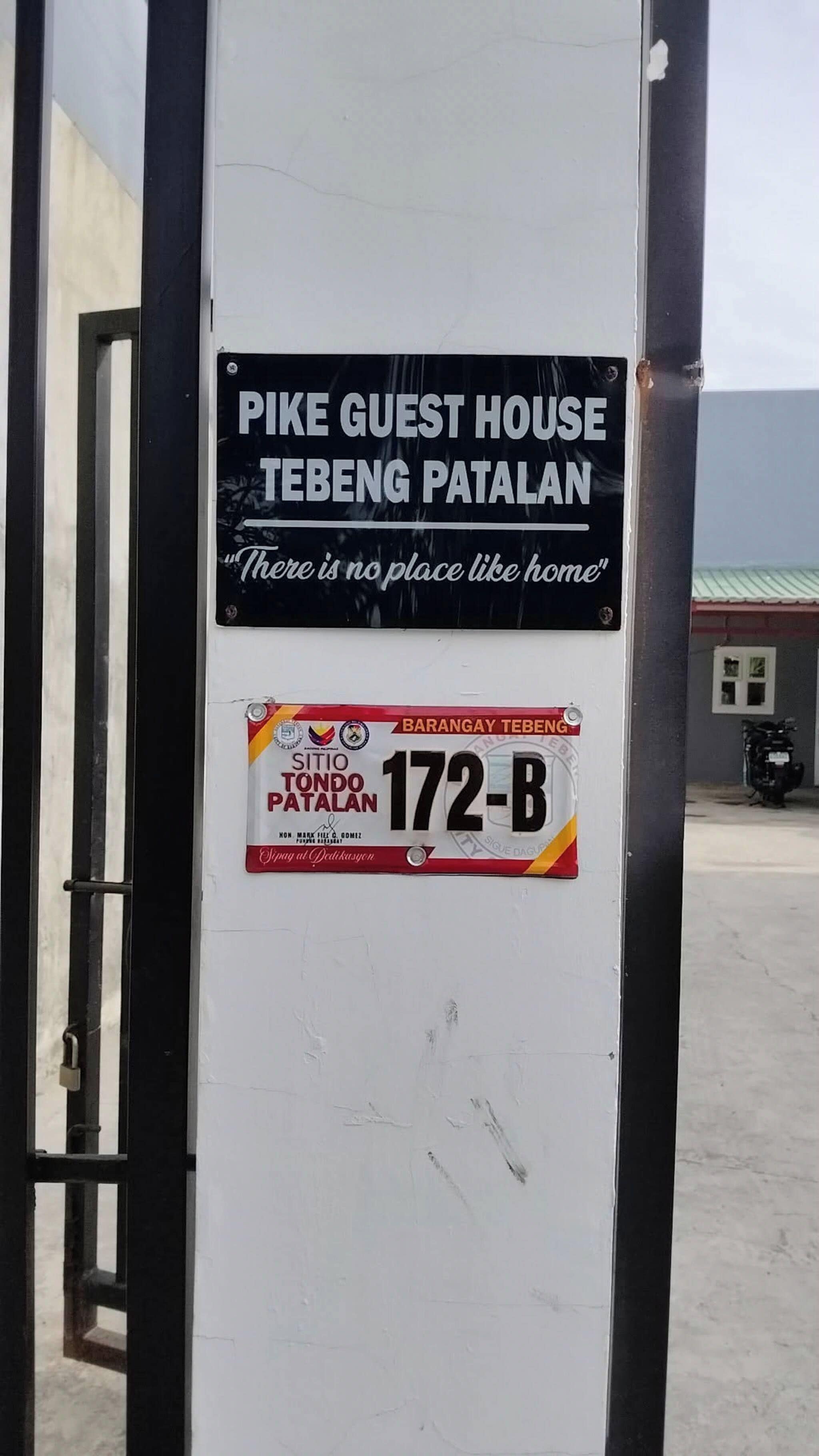 A sign for Pike Guest House Tebeng Patalan with a slogan and a parking permit sticker.