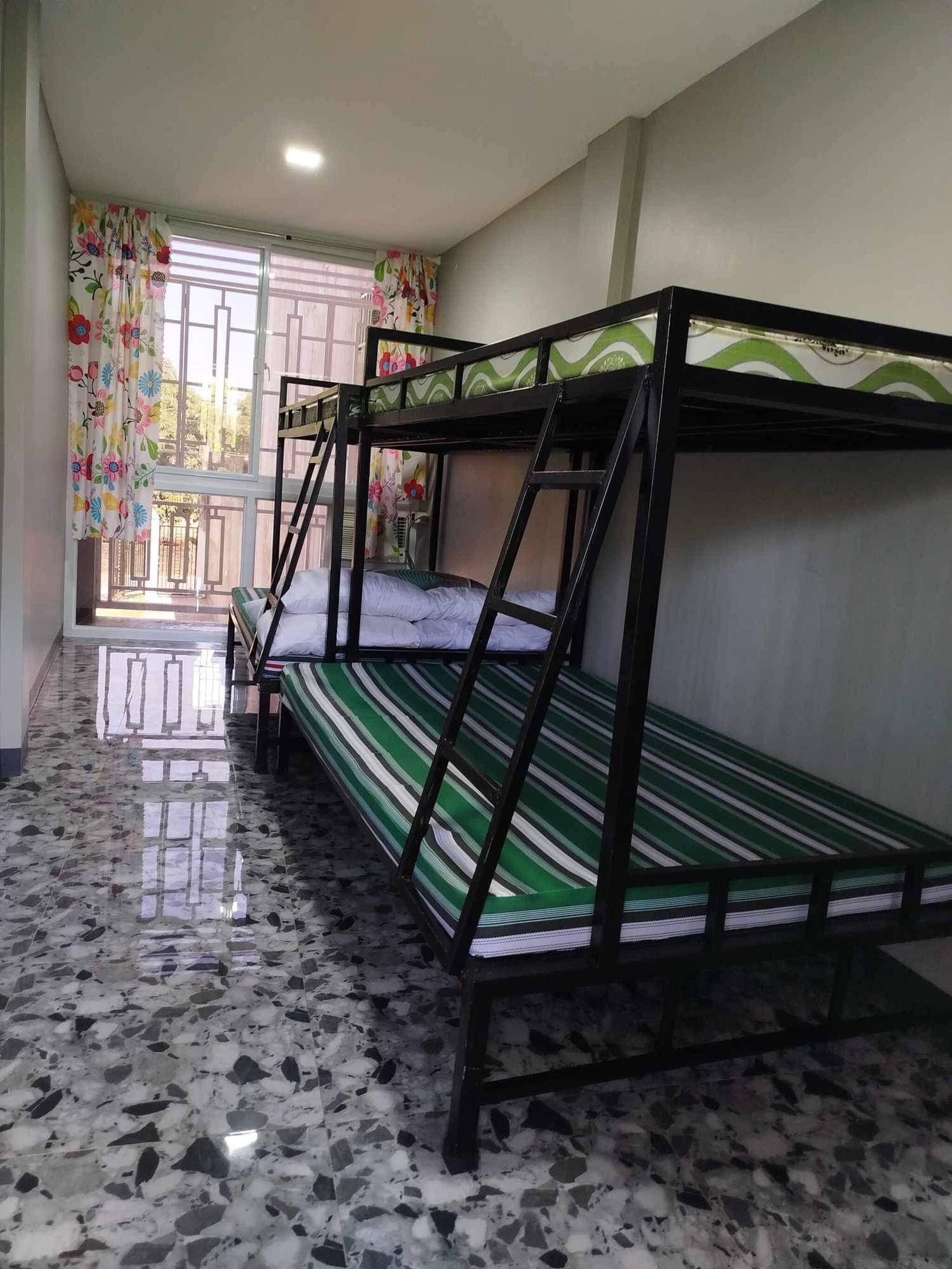 A dormitory room with bunk beds, a tiled floor, and a window with curtains.