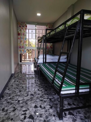Una habitación con literas, piso de baldosas y una ventana con cortinas estampadas.