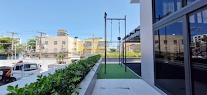 En balkon med grøn kunstgræs, en metal stang til træning og udsigt til bygninger samt en parkeret varevogn.