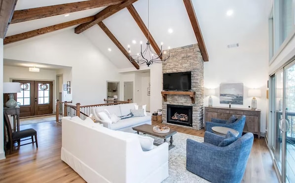 Un salon spacieux avec une cheminée, des canapés blancs, un fauteuil bleu et un mur d’accent en pierre.