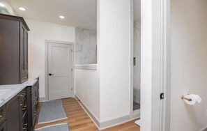 A hallway leading to a bathroom with a shower, a door with a towel hanging, and a marble backsplash.