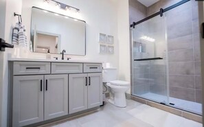 Une salle de bain moderne avec une douche à parois de verre, un grand miroir et un lavabo blanc.