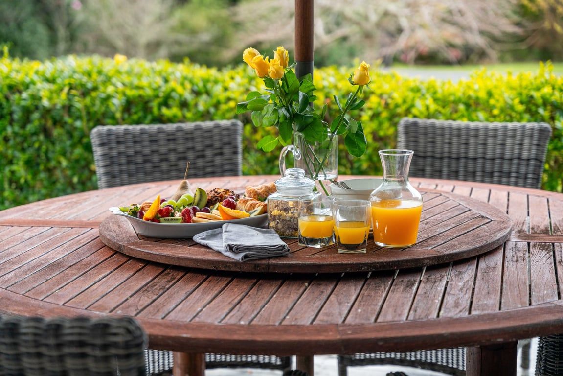 A round wooden table with breakfast items, a vase with yellow flowers, and a glass of orange juice.