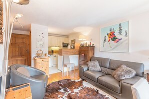 A modern living room with a leather sofa, a dining area with a wooden table, and a kitchen with white cabinets. - Le Cosy des Montagnes - Welkeys (Megève)