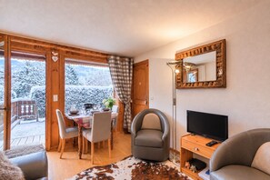 A cozy room with a dining table set for two, a comfortable armchair, a television, and a mirror on the wall. - Le Cosy des Montagnes - Welkeys (Megève)