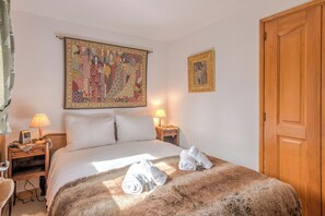 A hotel room with a large bed, two bedside tables with lamps, a wooden door, and two framed artworks on the wall. - Le Cosy des Montagnes - Welkeys (Megève)