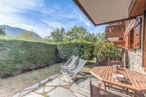A wooden deck with a table and chairs, a stone pathway, and a view of a mountain. - Le Cosy des Montagnes - Welkeys (Megève)