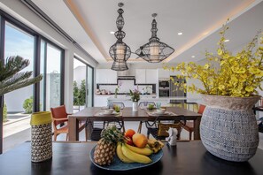A modern kitchen with white cabinets, a dining table set with plates, and a large vase with yellow flowers. - Villa Satori 3 Bed Seaview Infinity Pool (Bophut, Koh Samui)