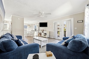 A living room with blue sofas, a white coffee table, and a ceiling fan. - Family Tides - Spacious 6BR Duplex, Two Full Floors w/ Private Balconies (Walk to Beach) (North Myrtle Beach)