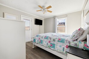 A bedroom with a bed, a ceiling fan, a TV, and a window. - Family Tides - Spacious 6BR Duplex, Two Full Floors w/ Private Balconies (Walk to Beach) (North Myrtle Beach)