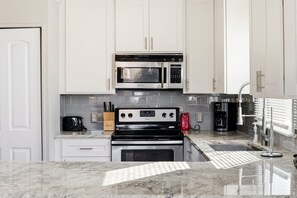 A modern kitchen with white cabinetry, a stainless steel microwave, a coffee maker, and a built-in oven. - Family Tides - Spacious 6BR Duplex, Two Full Floors w/ Private Balconies (Walk to Beach) (North Myrtle Beach)