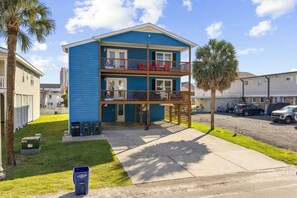 A two-story building with a blue exterior, a balcony on the second floor, and a parking area in front. - Family Tides: Unit 1 - Comfy 3BR Unit w/ Private Balcony (Walk to Beach) (North Myrtle Beach)