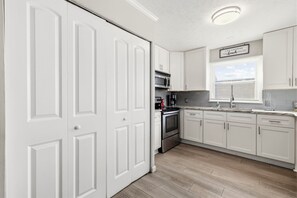 A modern kitchen with white cabinetry, a built-in oven, a microwave, and a coffee maker. - Family Tides: Unit 1 - Comfy 3BR Unit w/ Private Balcony (Walk to Beach) (North Myrtle Beach)