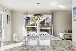 A dining area with a marble table, white chairs, a hanging light fixture, and a view of a building with balconies. - Family Tides: Unit 2 - Comfy 3BR Unit w/ Private Balcony (Walk to Beach) (North Myrtle Beach)