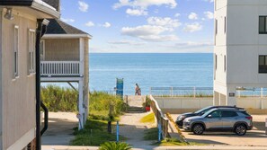 Um imóvel à beira-mar com um caminho que leva ao mar, um carro estacionado e um edifício com varanda.