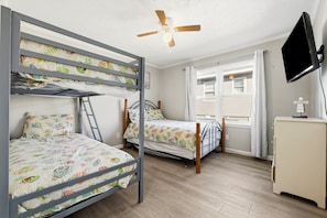 A room with bunk beds, a ceiling fan, a television, and a window with curtains. - Family Tides: Unit 2 - Comfy 3BR Unit w/ Private Balcony (Walk to Beach) (North Myrtle Beach)