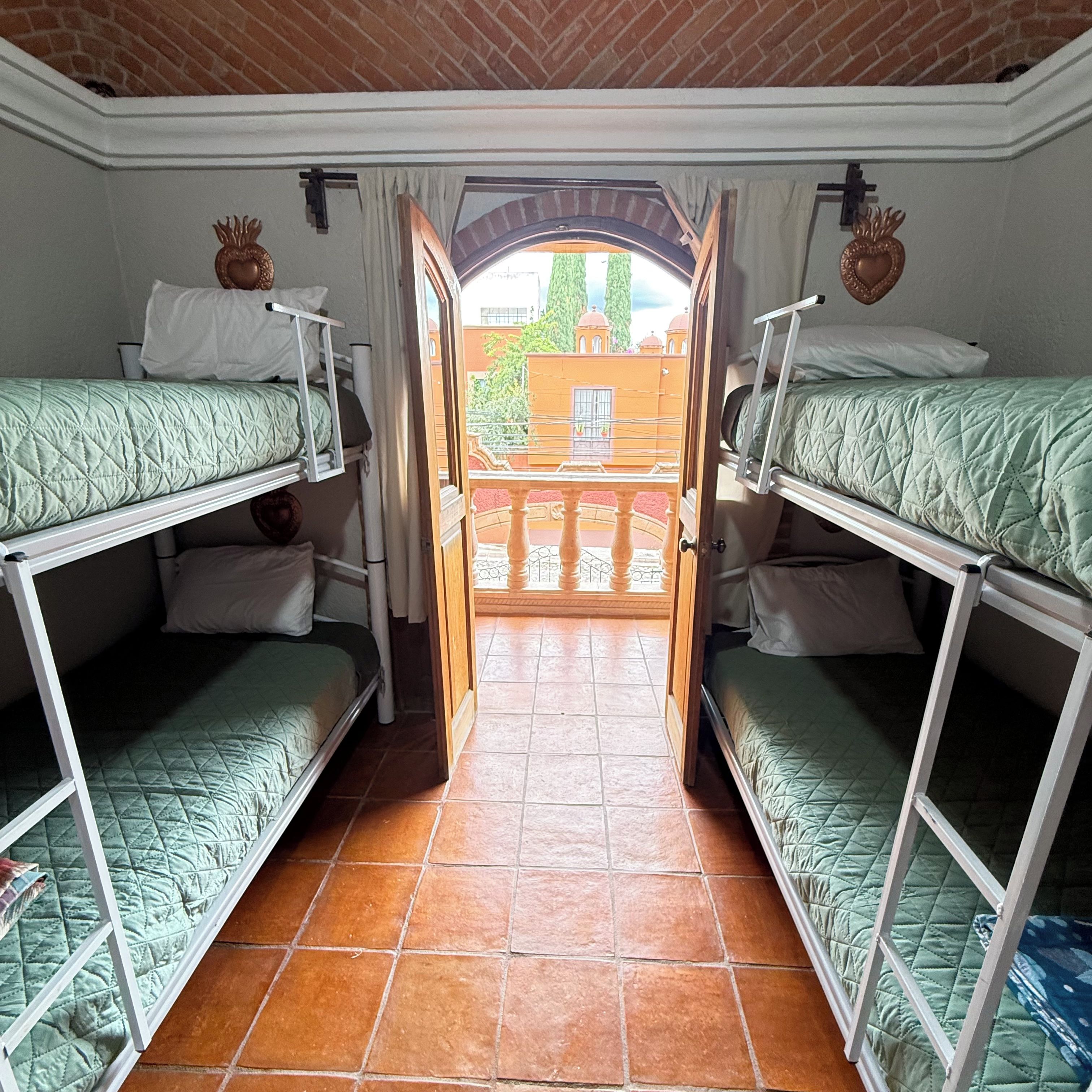 Una habitación con literas, suelo de baldosas y una puerta abierta que da a un balcón exterior.