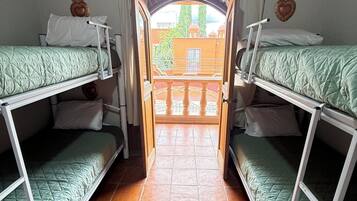 Una habitación con literas, suelo de baldosas y una puerta abierta que da a un balcón exterior.